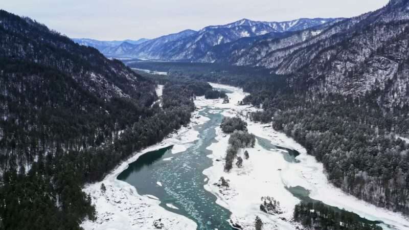 Aerial view of a Bavarian river in winter, showing snow-covered banks and icy water under a clear blue sky.