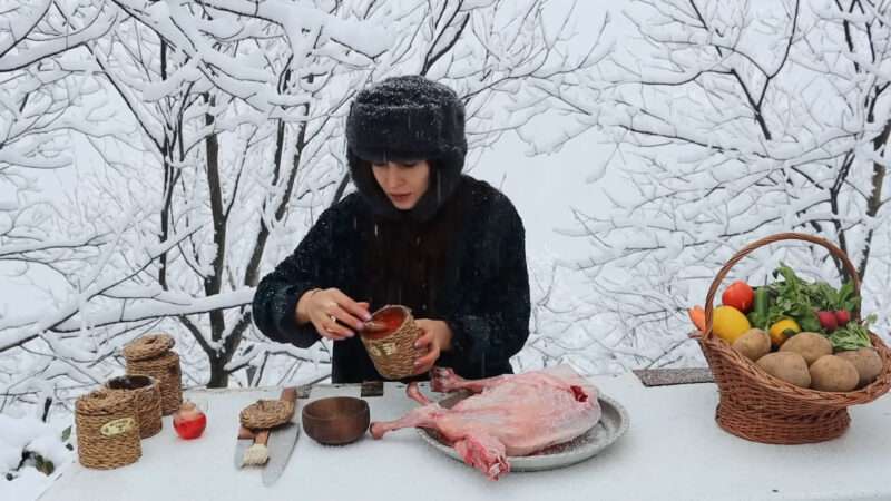 A woman is seen preparing food in a snowy environment, highlighting her resourcefulness and dedication to cooking outdoors.