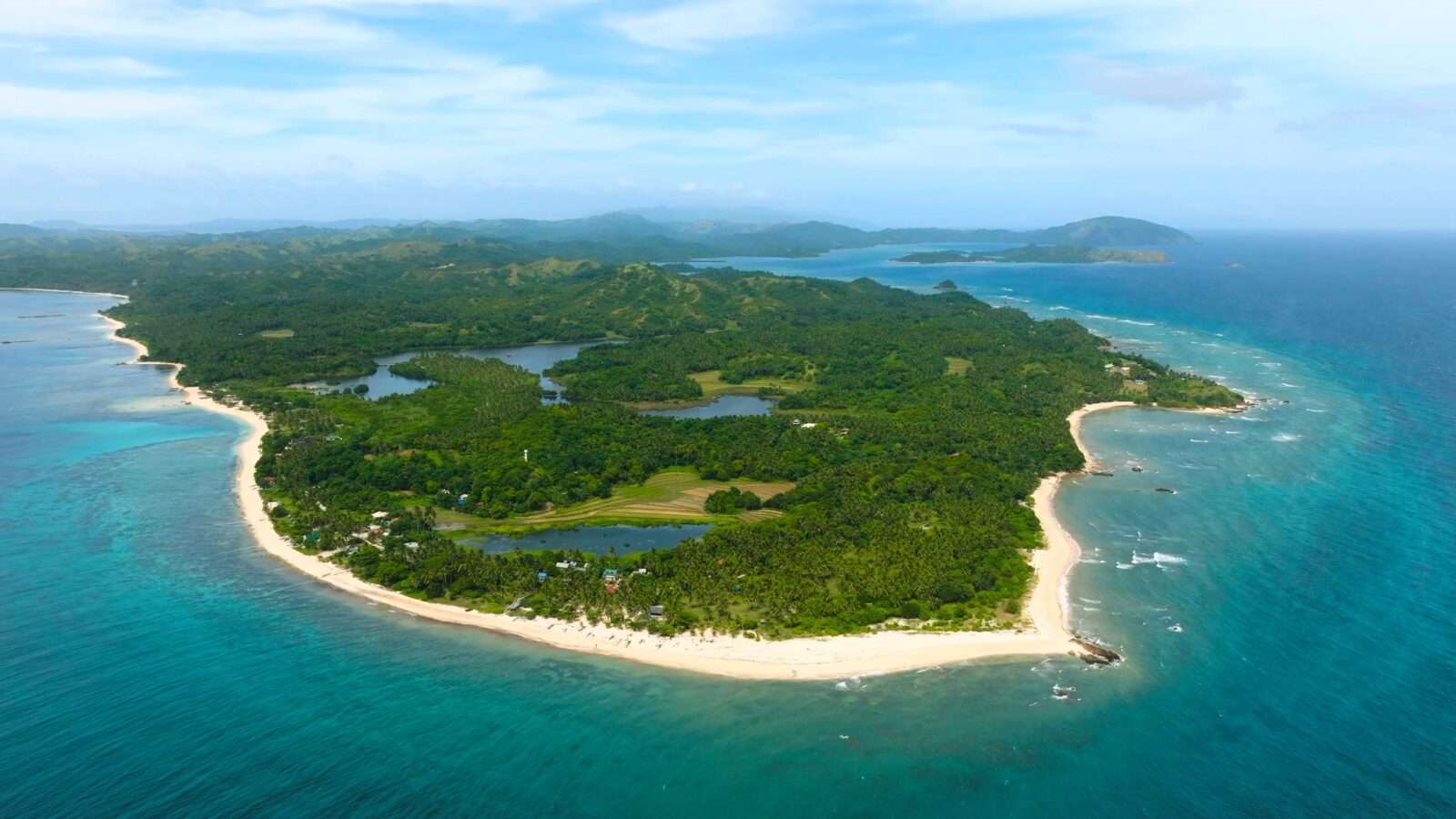 Aerial view of the lush green island, one of the world's natural wonders, surrounded by a turquoise ocean. It has sandy beaches, small lakes and distant hills shining under the clear sky
