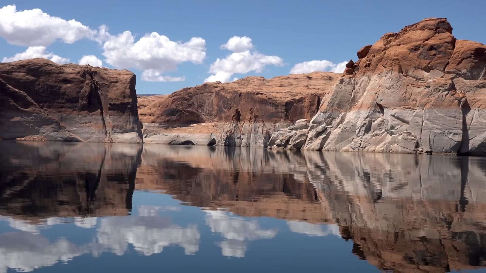 Three people are standing high on a mountain looking out at a blue lake, Wonders of the World Pictures.
