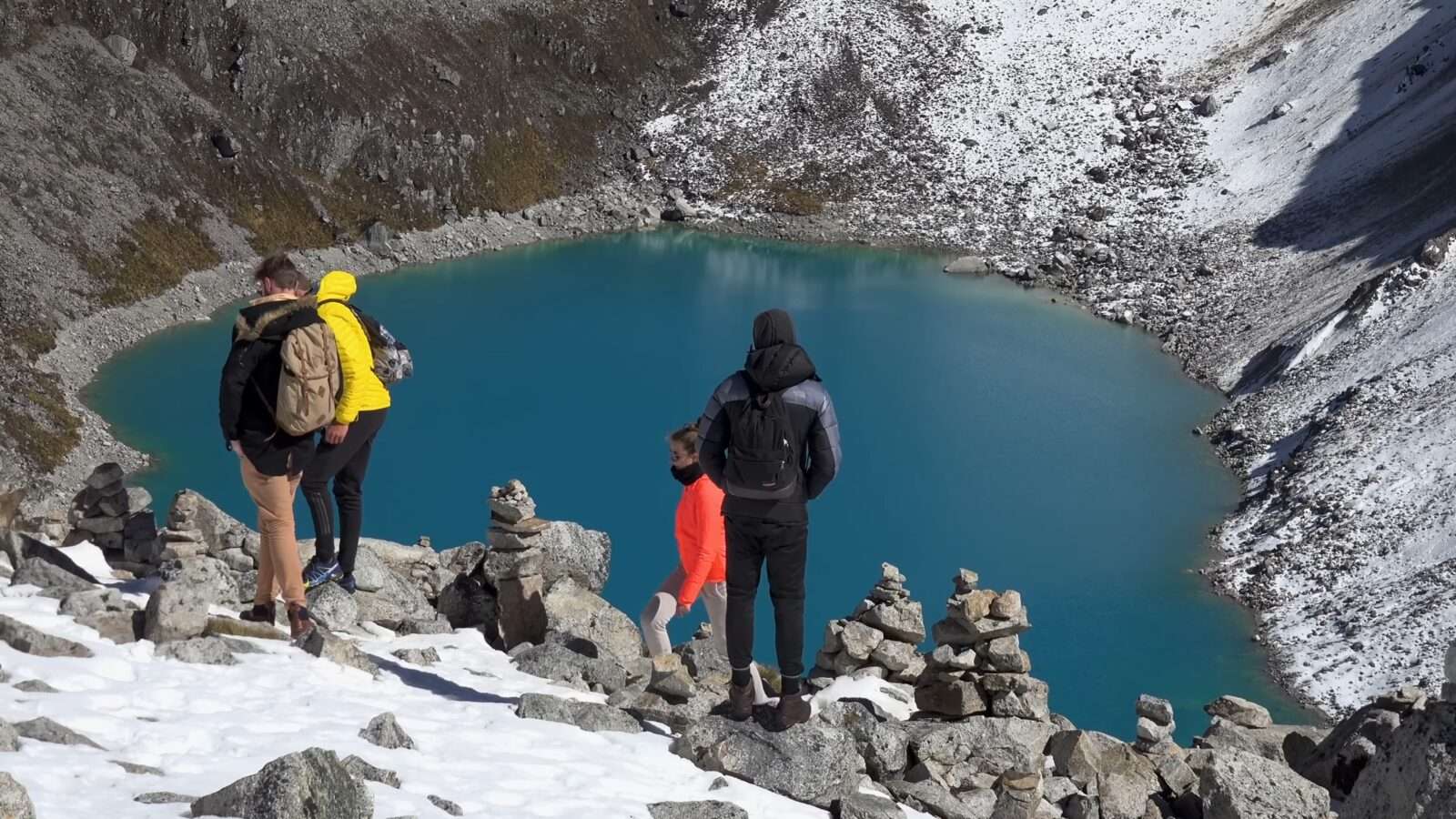 Three people are standing high on a mountain looking out at a blue lake, Wonders of the World Pictures.