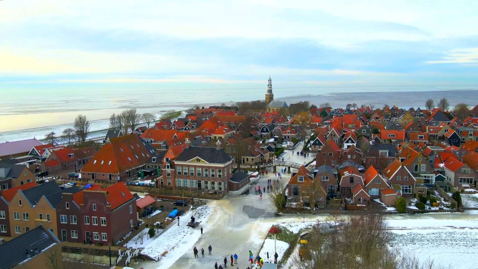 An aerial view of a snow-covered village, with colourful houses and people ice skating on a frozen canal, Wonders of the World Pictures.
