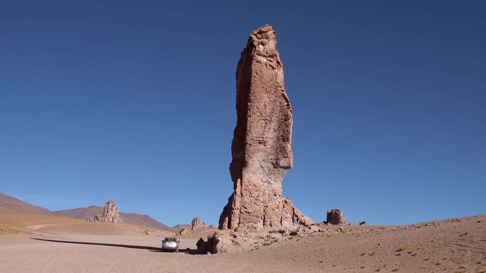 Picture of a car parked next to a huge rock in the desert, Wonders of the World Pictures.
