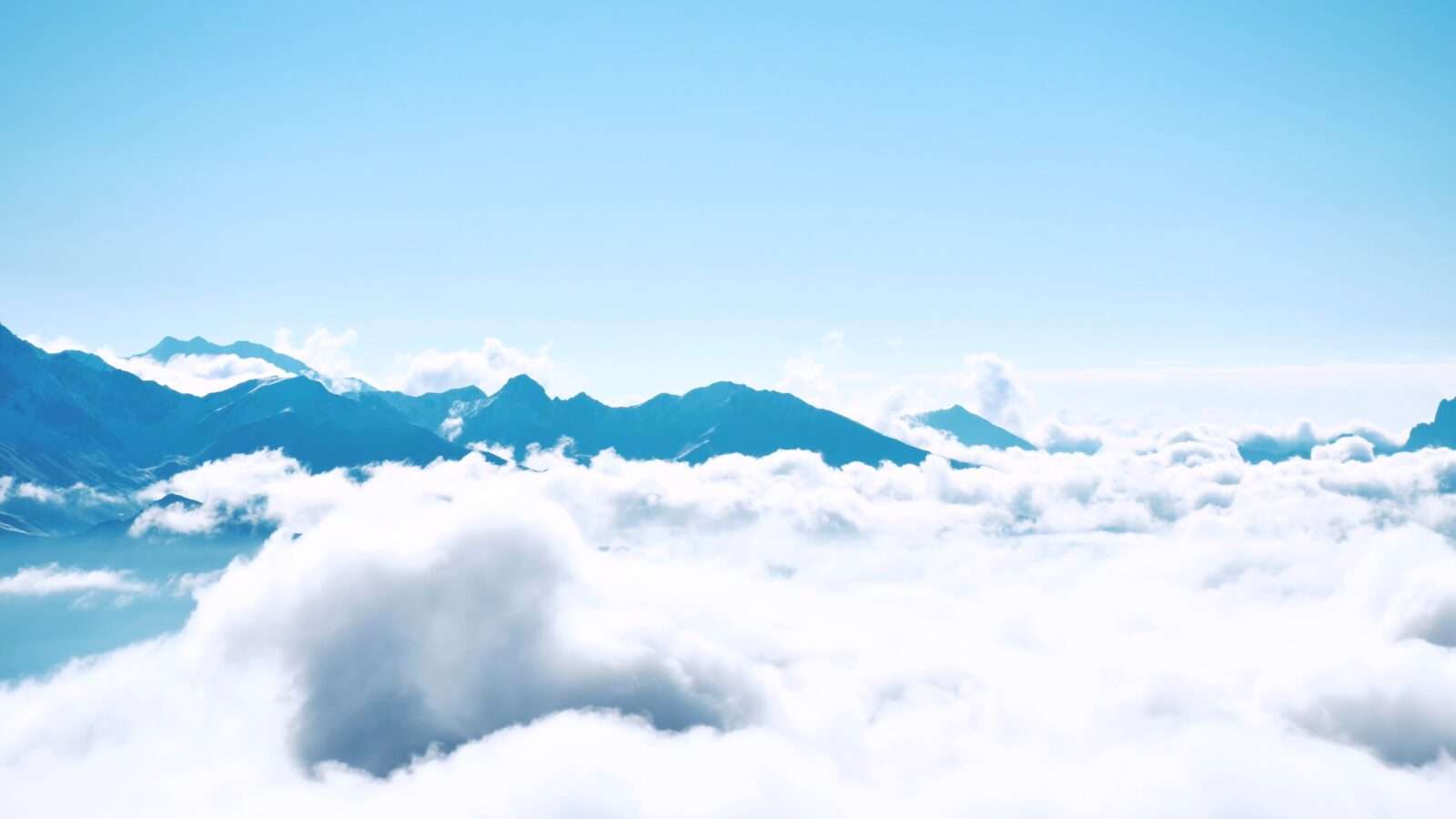 Aerial view of majestic mountains partially covered by light clouds against a clear blue sky, Wonders of the World Pictures.
