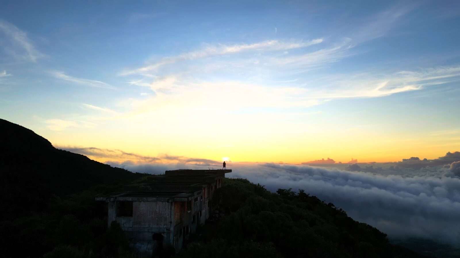 A man is standing on the top of a building, enjoying the view of the clouds, Wonders of the World Pictures.
