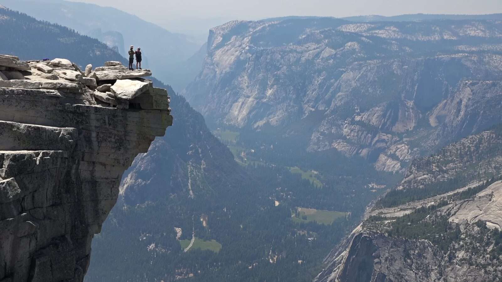 A man stands at the edge of a cliff, observing the view across the valley, Wonders of the World Pictures.