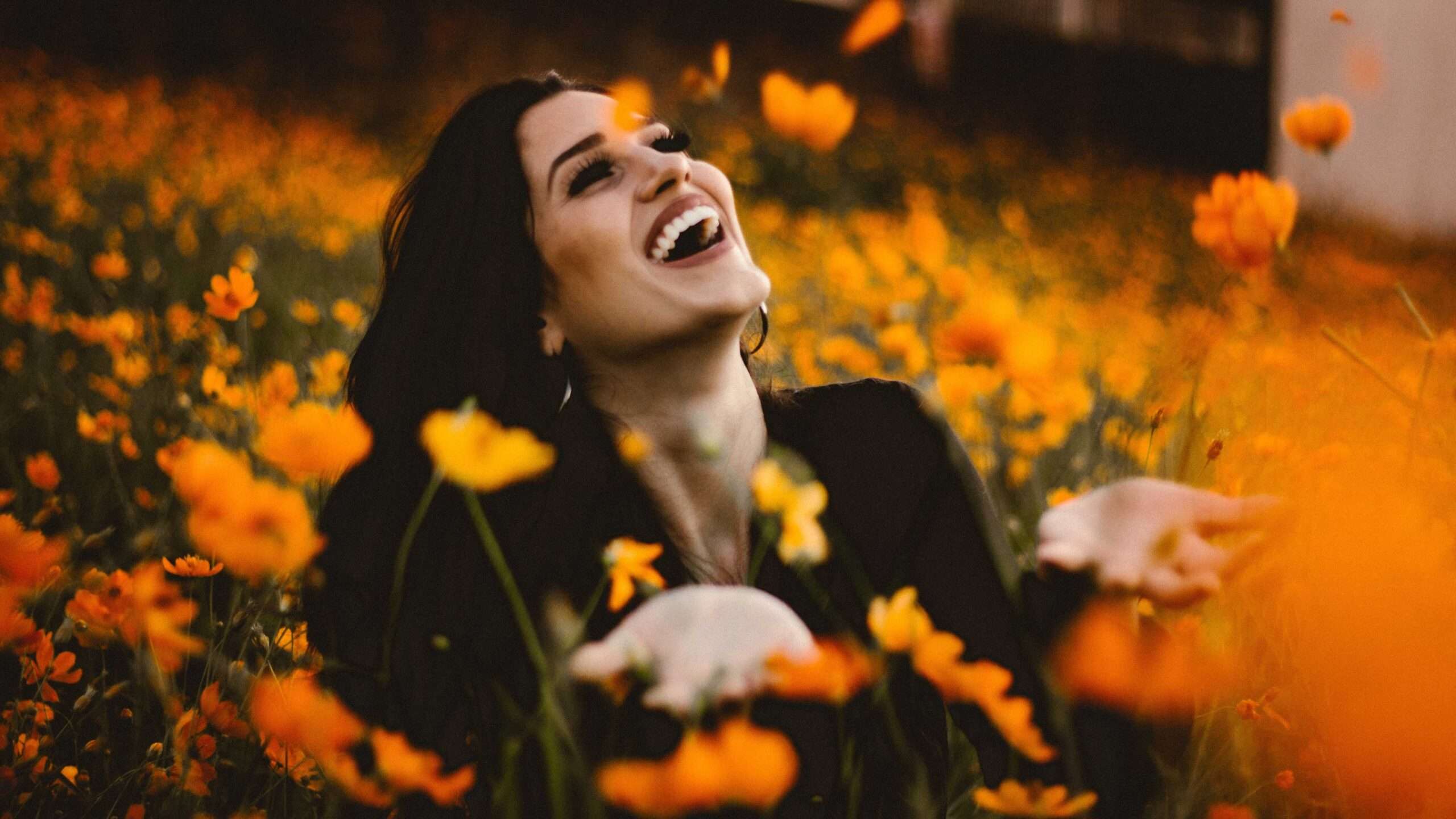 Woman joyfully laughing in a vibrant field of orange flowers, emphasizing happiness and nature's beauty.