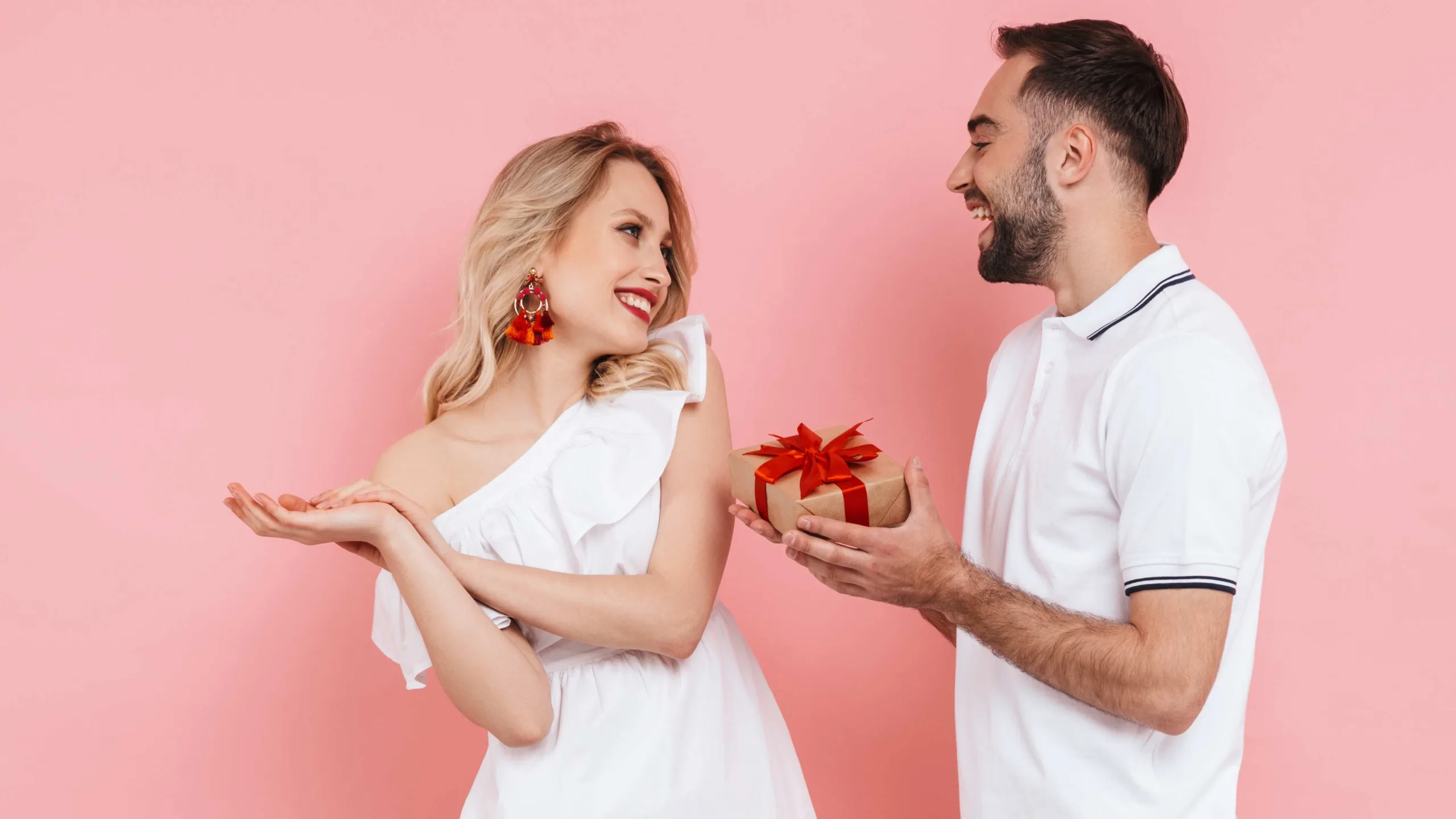 Image of smiling couple with gift box on pink background